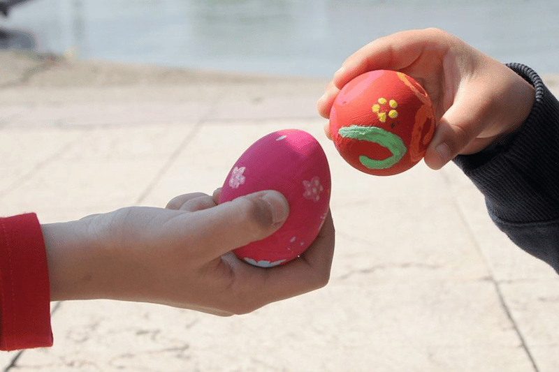 Ťukání vajíček, zdobené kraslice a dvě dětské ruce v detailu. 