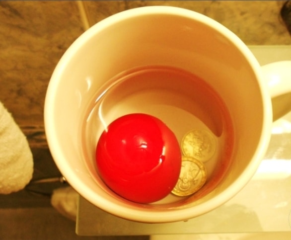 Hrníček s červeným vajíčkem, mincemi a vodou.