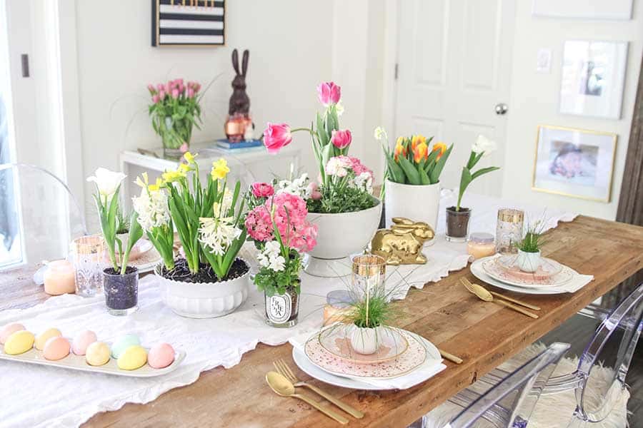 Prostřený stůl s jarními květinami, vajíčky a zlatou soškou zajíčka