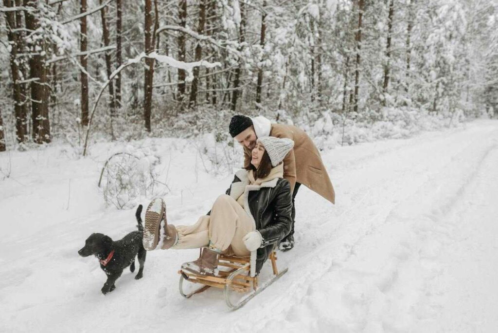 Usmívající se veselý pár se psem na saních v zasněžené přírodě.
